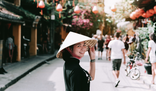 A young Asian woman wearing Vietnamese hat and smiling to the camera on a village street In Vietnam