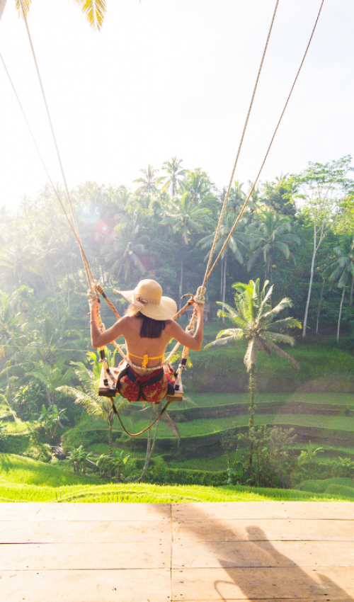 Person on Ubud Swing overlooking rice paddies, Bali, Indonesia, bathed in golden sunlight.